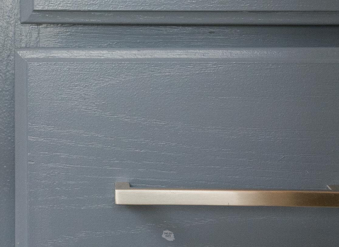 zoomed in view of painted charcoal blue bathroom cabinet with silver handle.