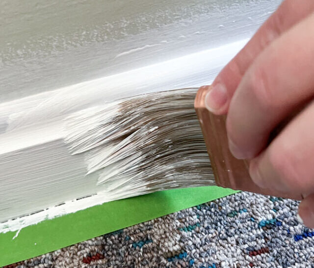 hand holding brush apply white paint to molding.