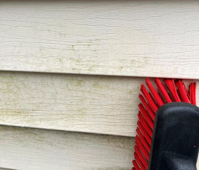 red soft brush cleaning dirty vinyl siding after vinegar water spray on it.