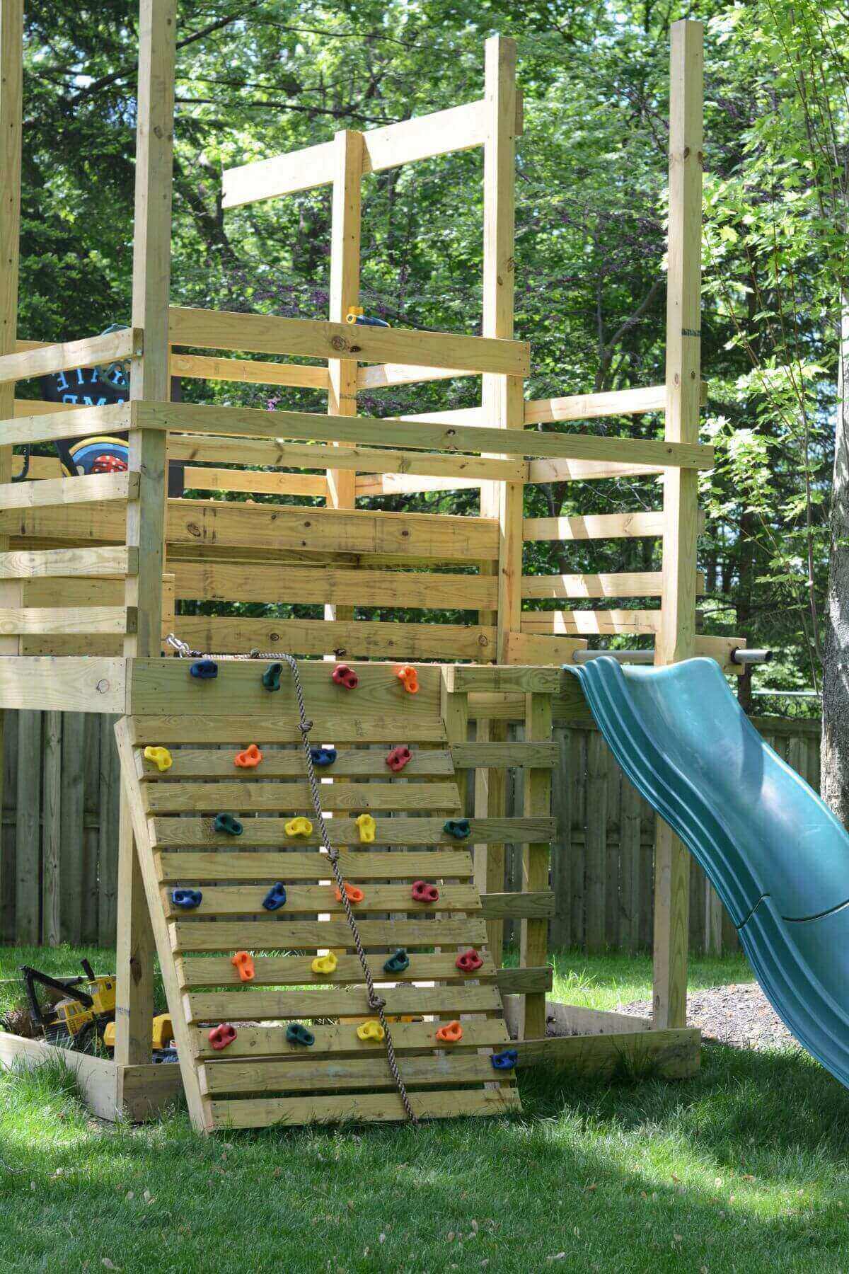 DIY wooden playset with rockwall, green slide and rope.