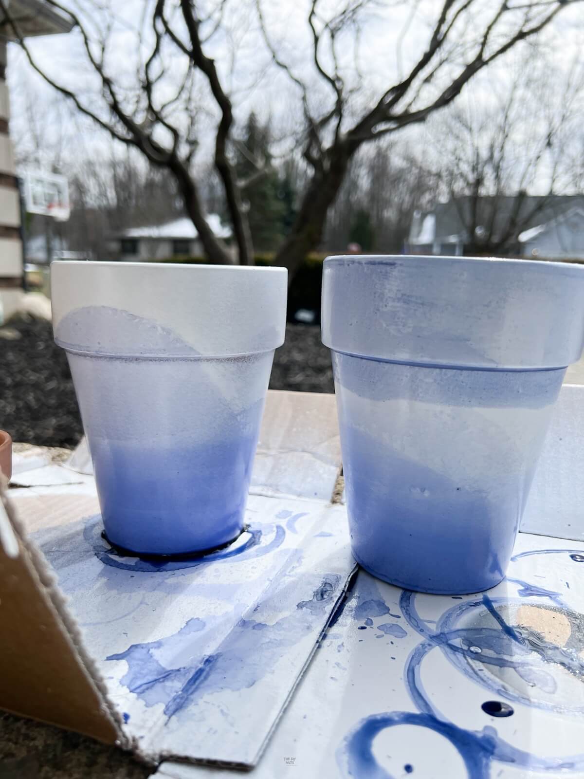 painted flower pots drying on cardboard outside.