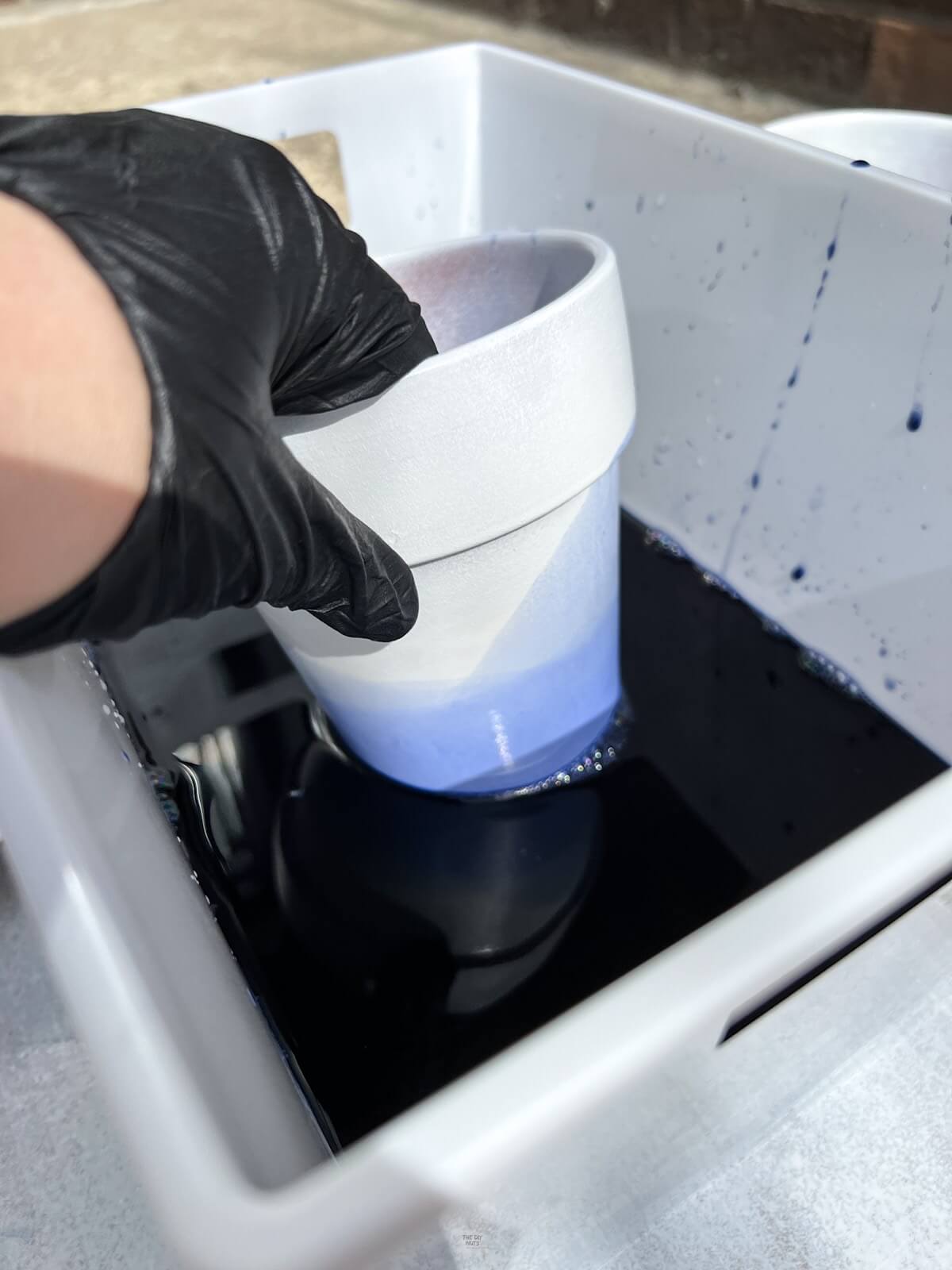 painted flower pot being dipped into blue dyed water.