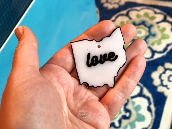 hand holding small ohio shaped white plastic shrinky dink with love written.