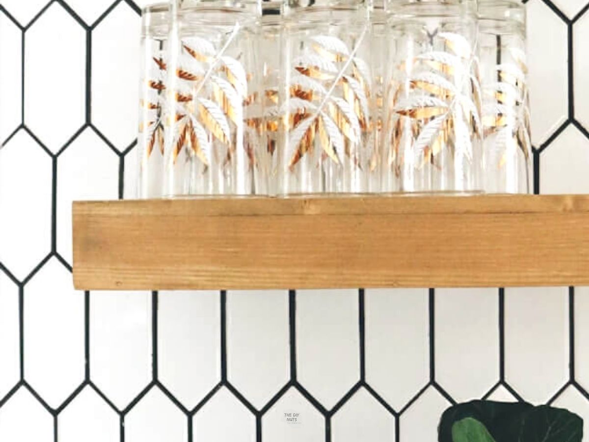 white geometric backsplash with black grout and glasses on wooden floating shelf.