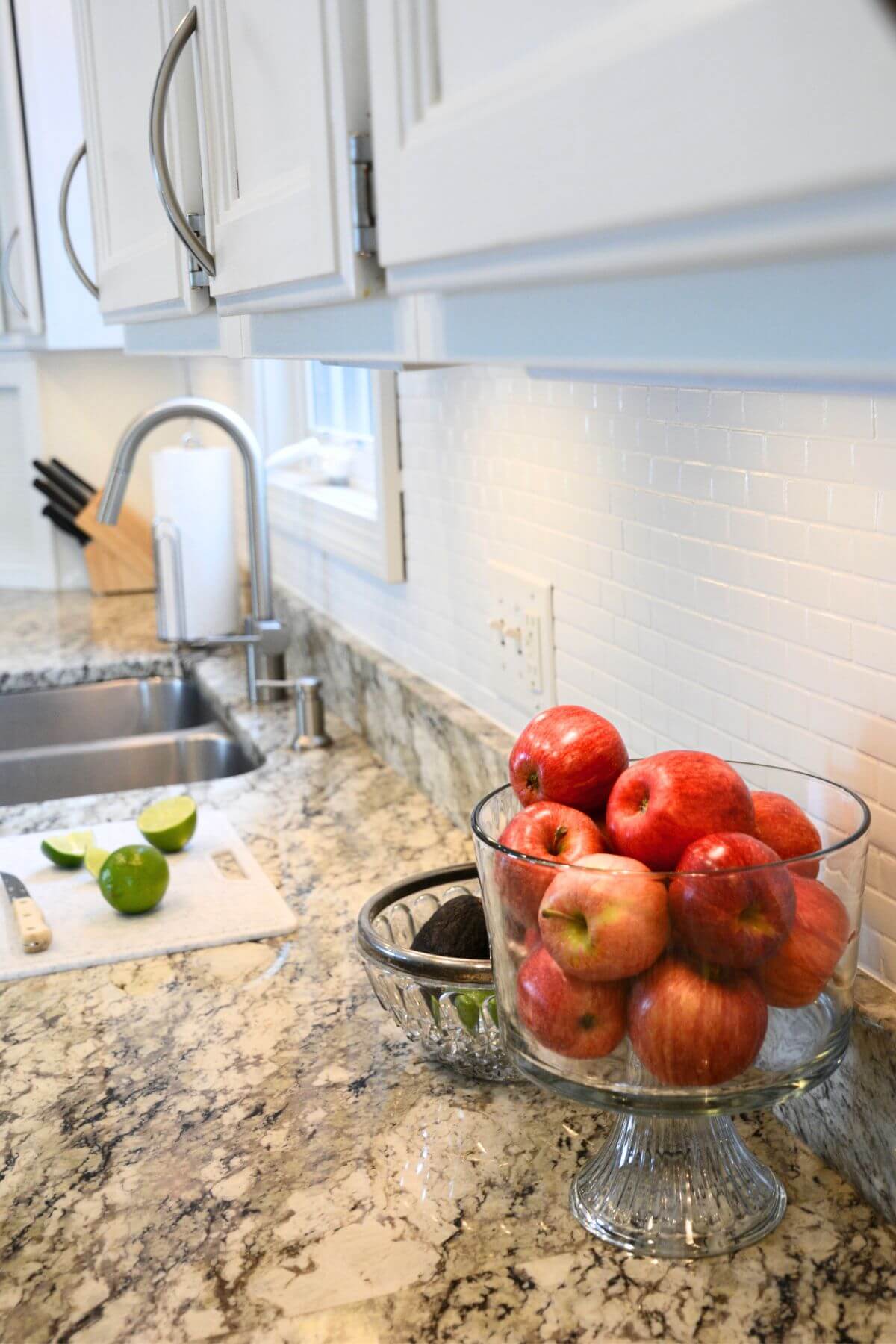granite counters with white cabinets, backsplash and red apples in a glass dish.