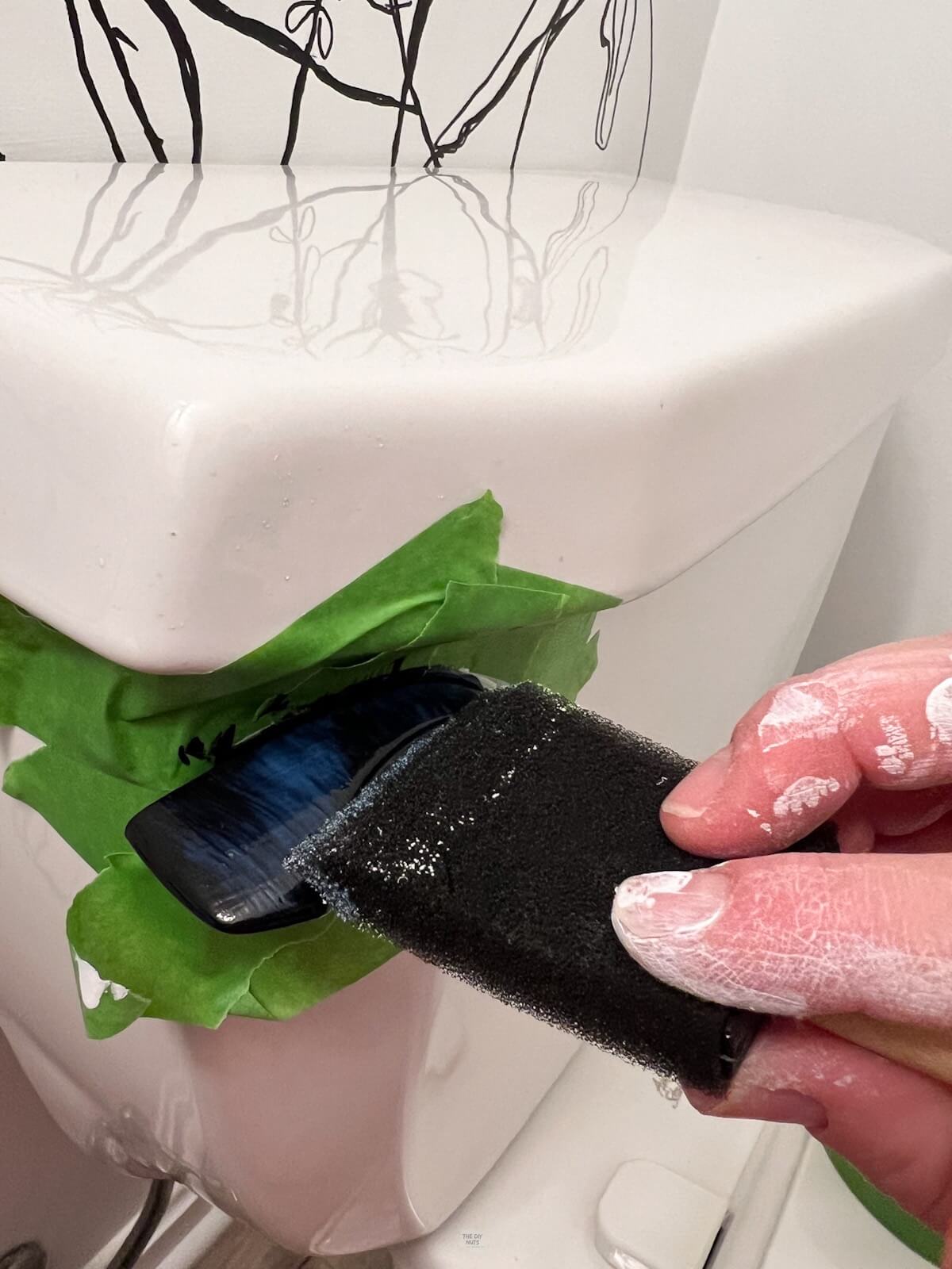 hand holding foam brush adding clear coat to black toilet flush.