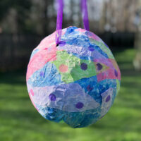 colorful homemade piñata made from a balloon hanging outside.