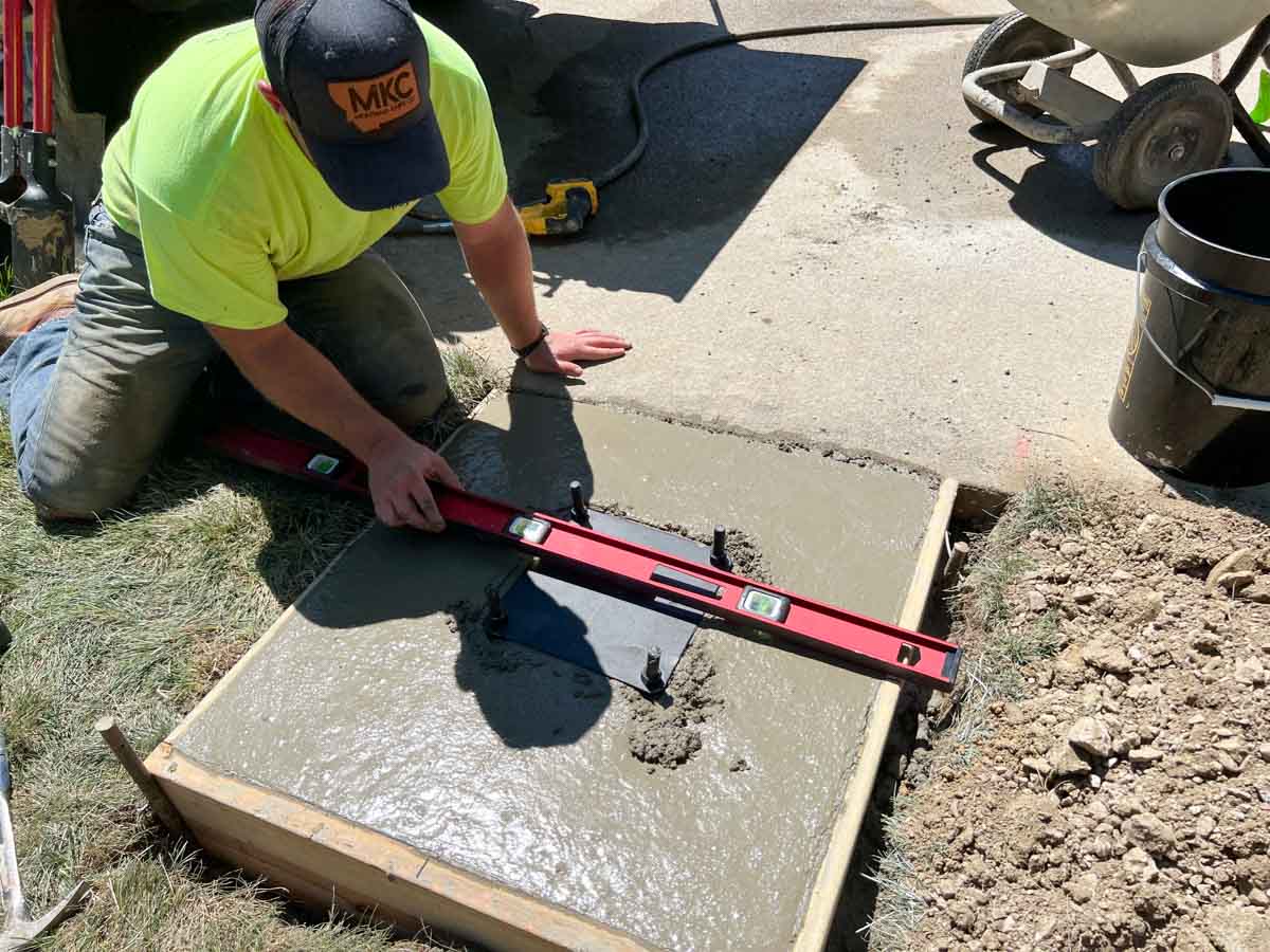 man holding level on top of black metal plate in concrete.