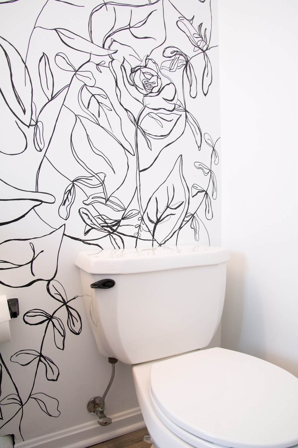 white toilet with black flush handle and hand drawn accent wall.