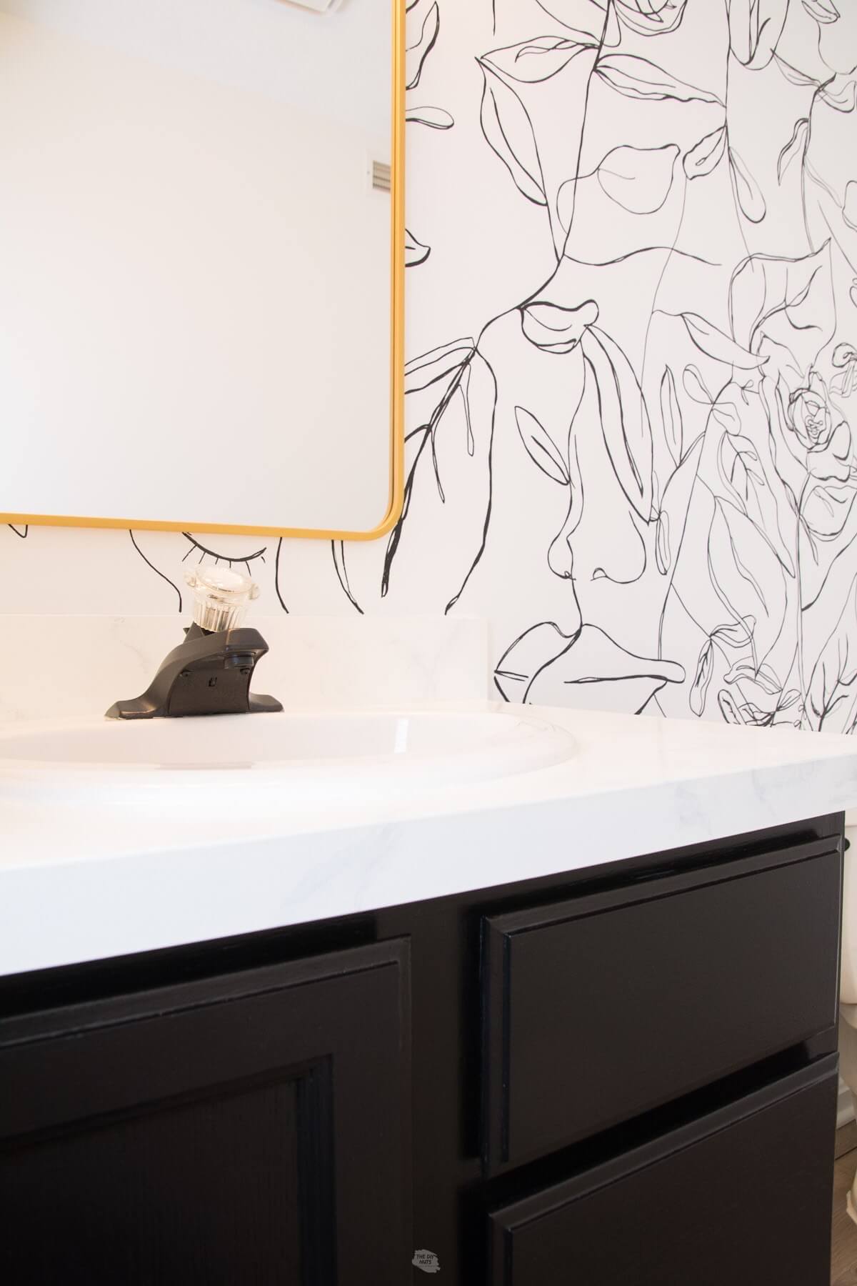black painted bathroom cabinets with gold mirror and black and white paint pen wall.