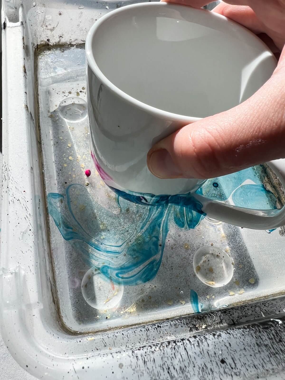 hand dipping mug in water with nail polish on top.