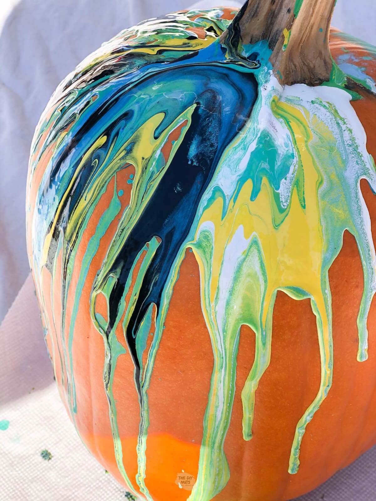Paint pour pumpkin with blue, teal, yellow, white and black marble effect.