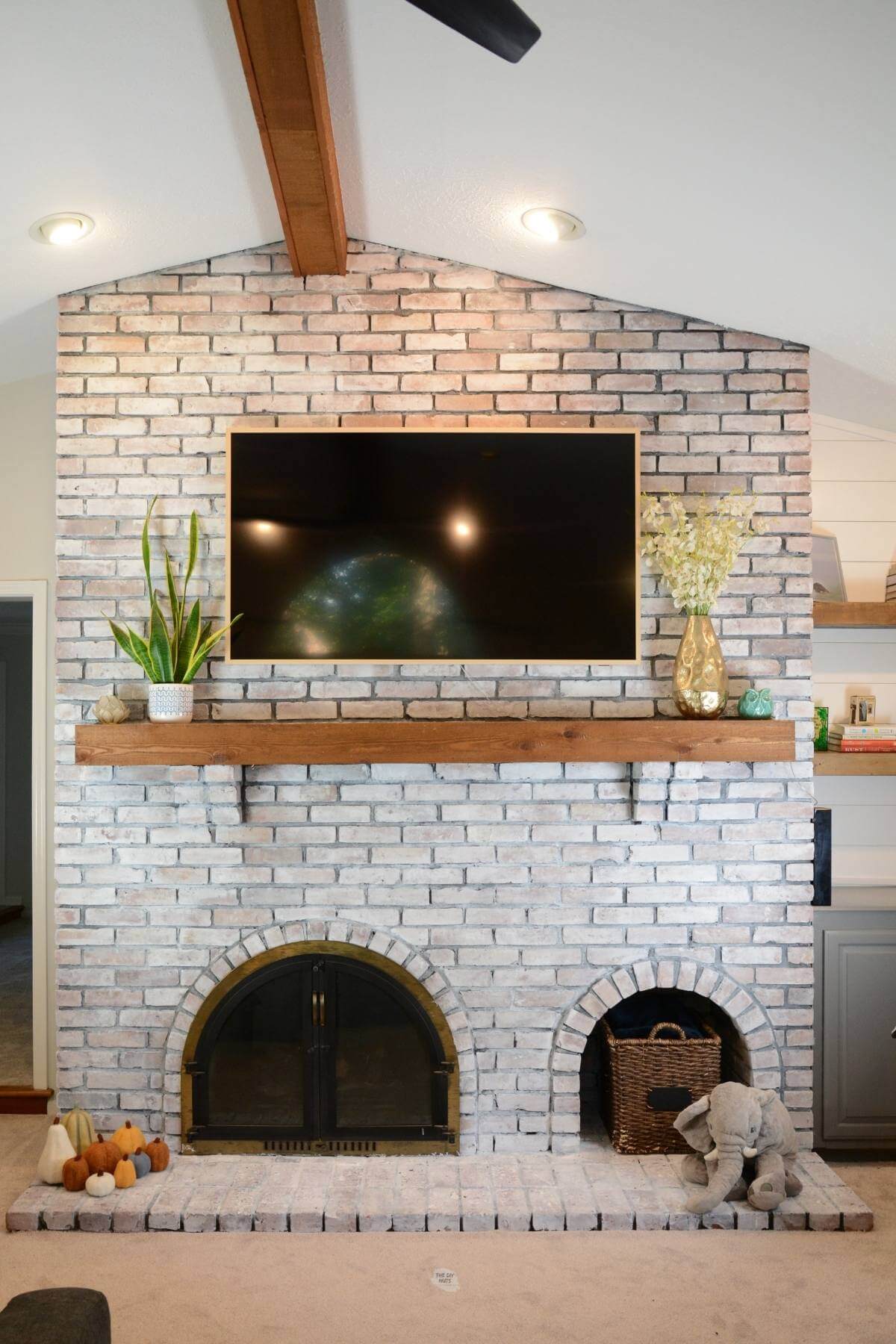 Final white washed large brick fireplace with wood beam and shelves.