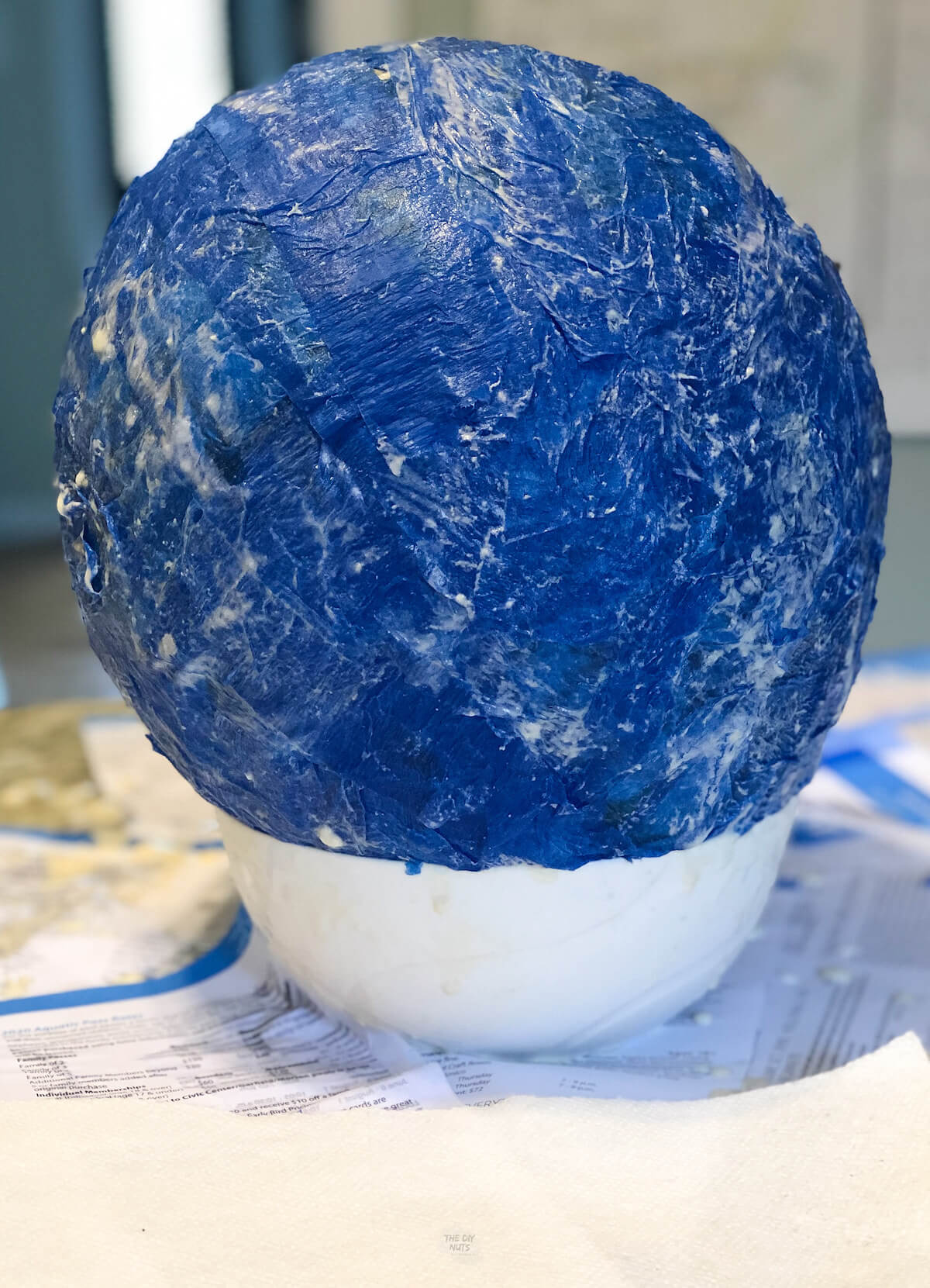 homemade blue piñata sitting on bowl with wet paper mache on it.