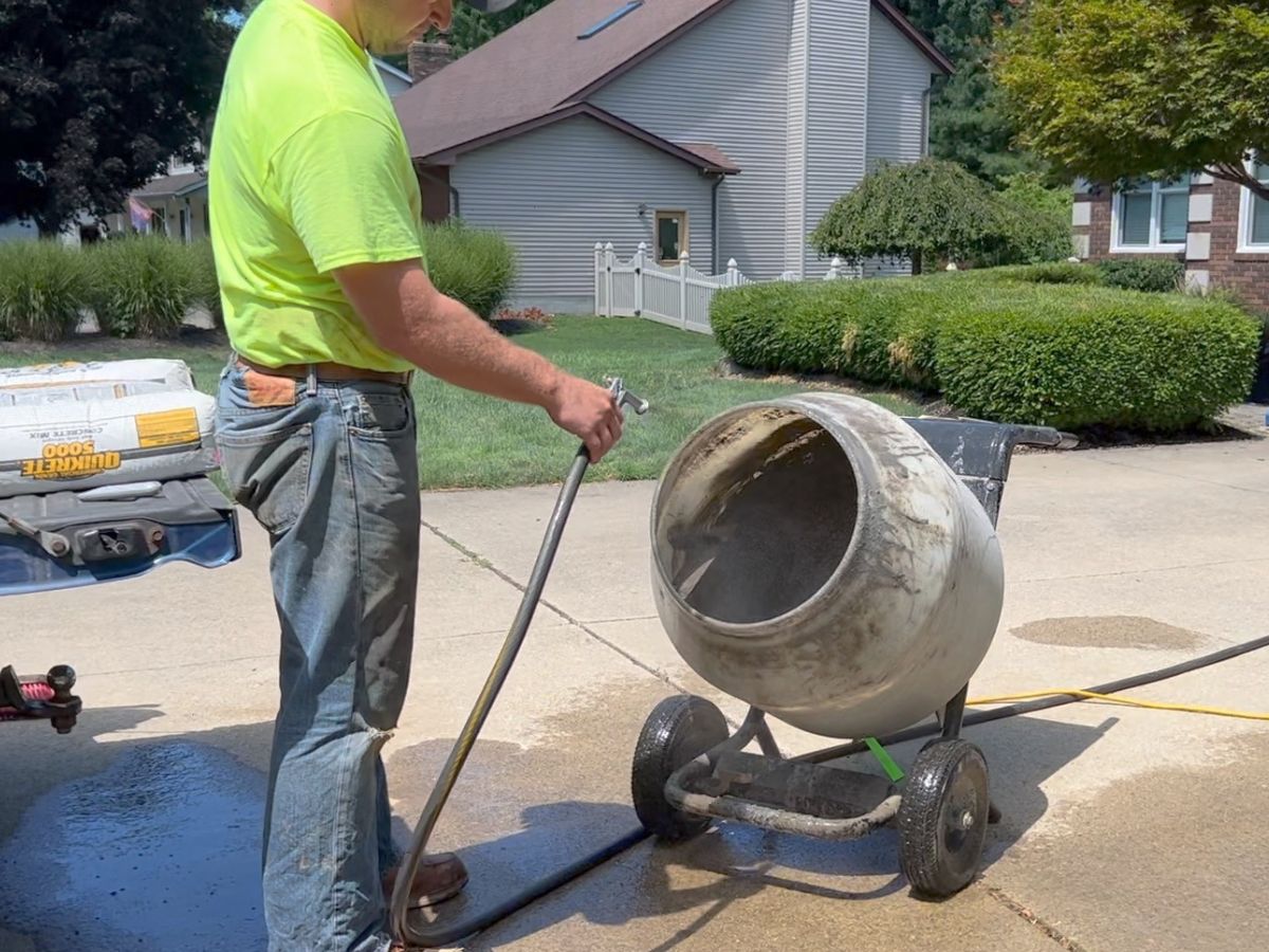 man spraying water into barrel concrete mixer.