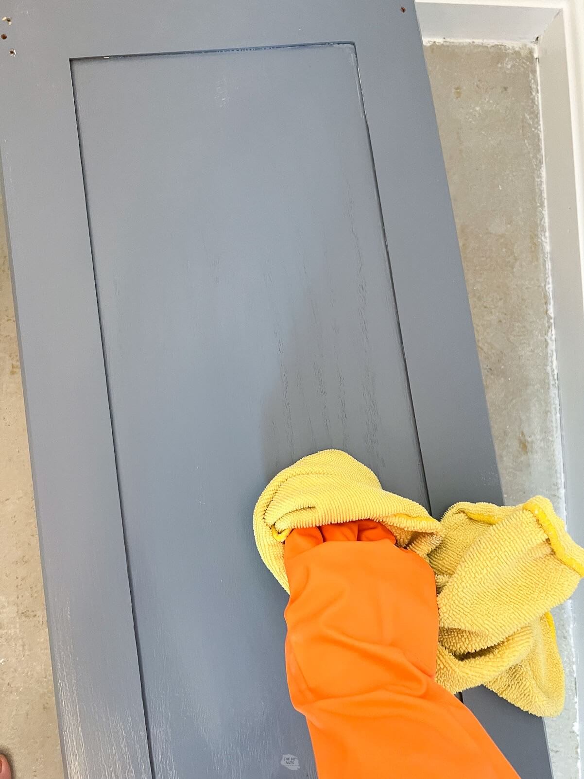 orange gloved hand holding yellow rag wiping painted cabinet door.