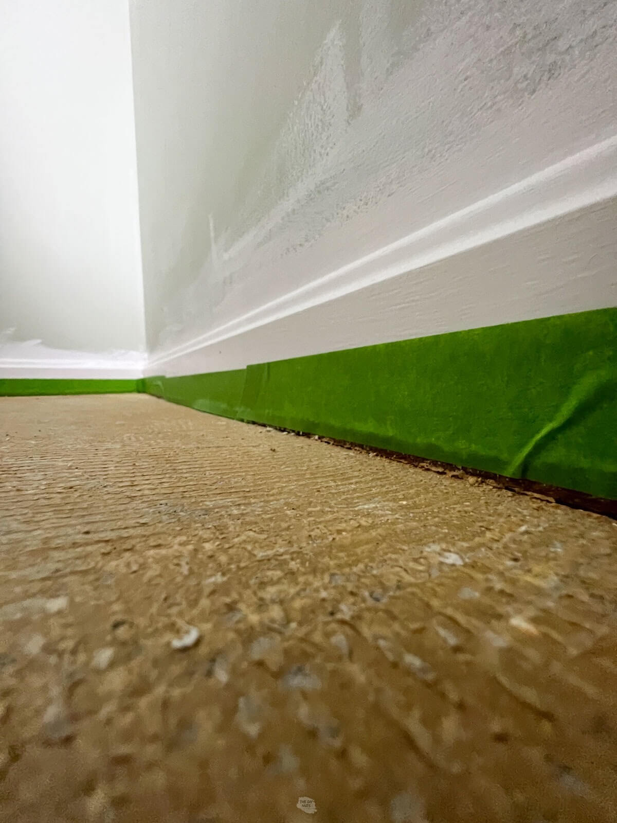 green painter's tape on white painted baseboards with carpet glue on floor.