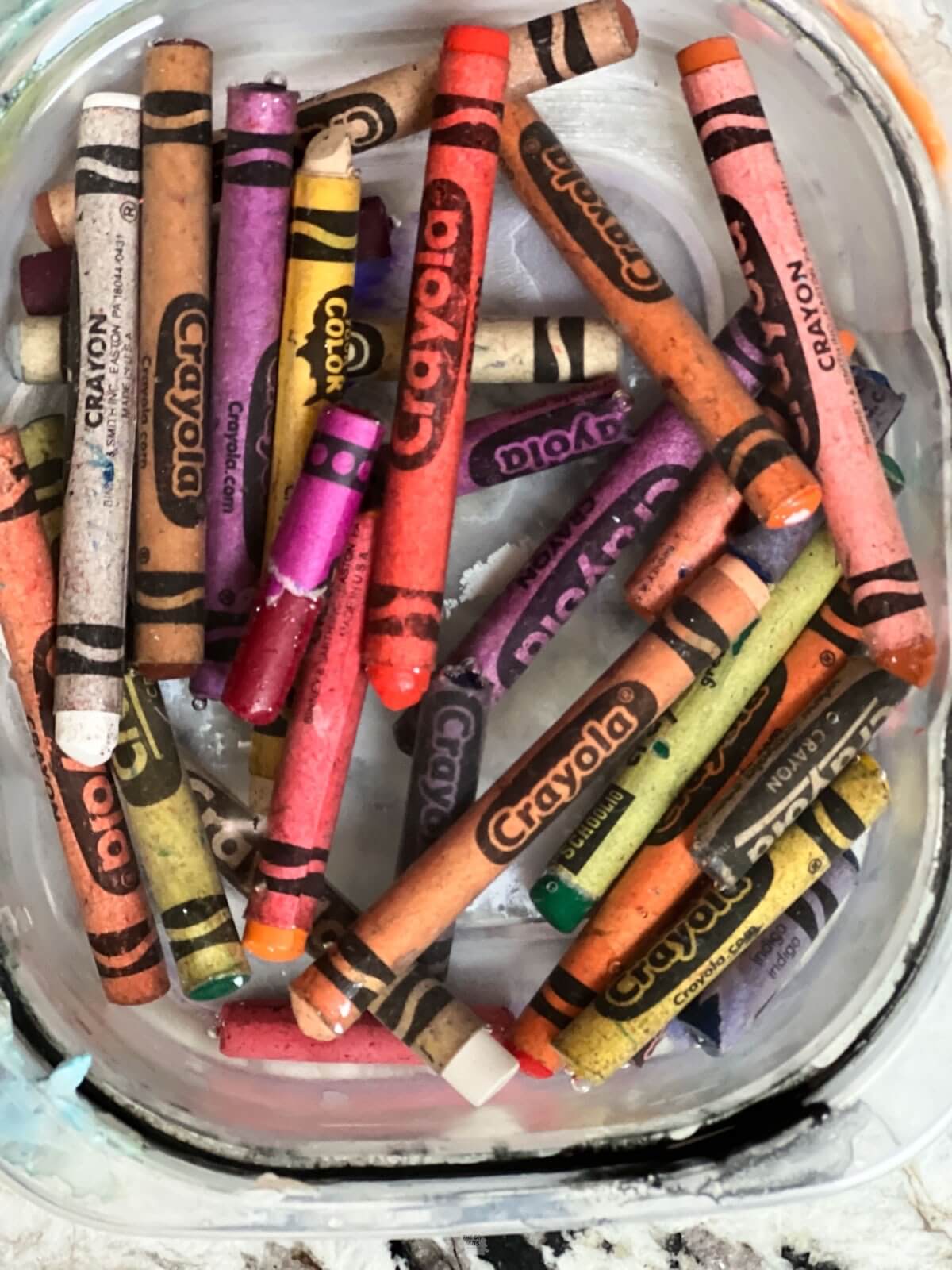 crayons soaking in water in small plastic container.