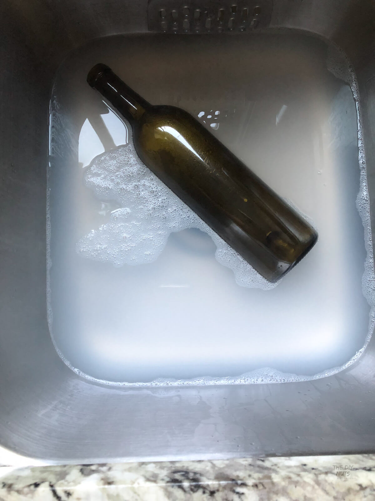 wine bottle with label being soaked in boiling water to remove label in stainless steel sink