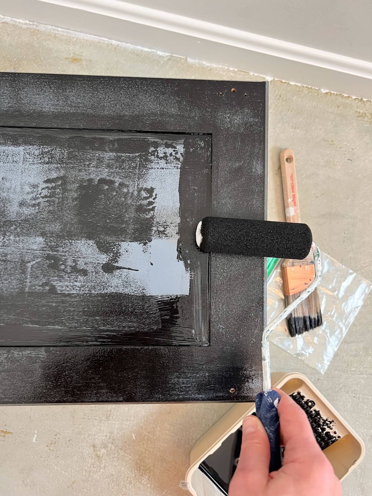 small foam roller painting the back of cabinet door with black paint.