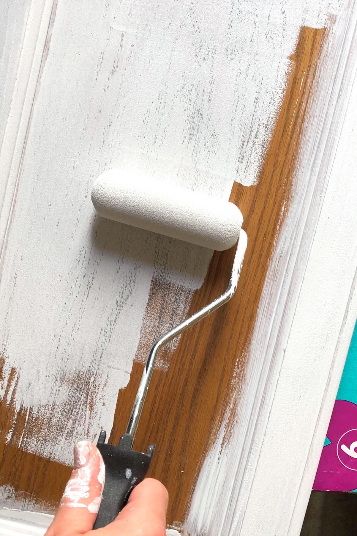 small foam roller applying white primer to oak cabinet door.