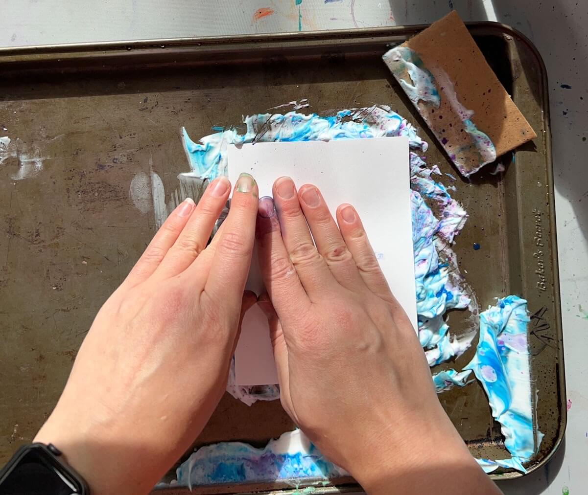 hand pushing paper into colored shaving cream.