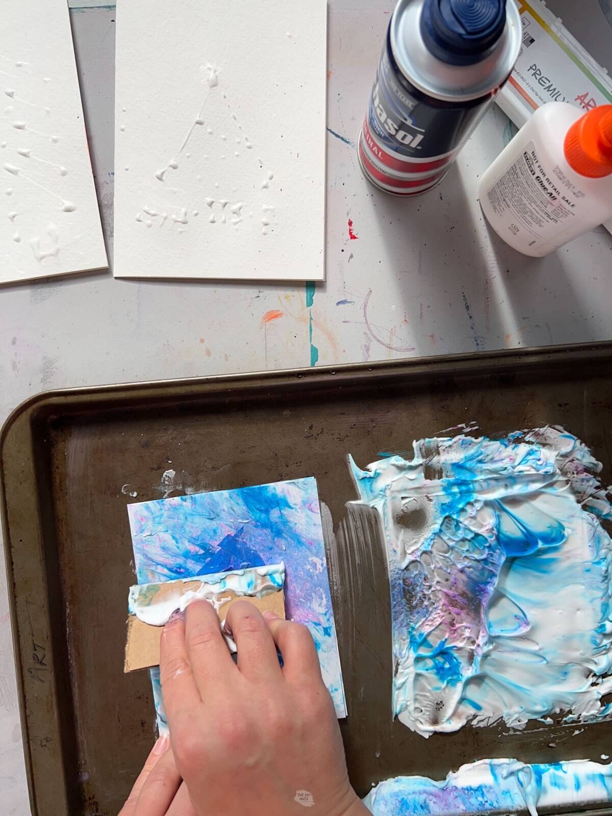 hand holding cardboard and scraping blue and purple shaving cream off.