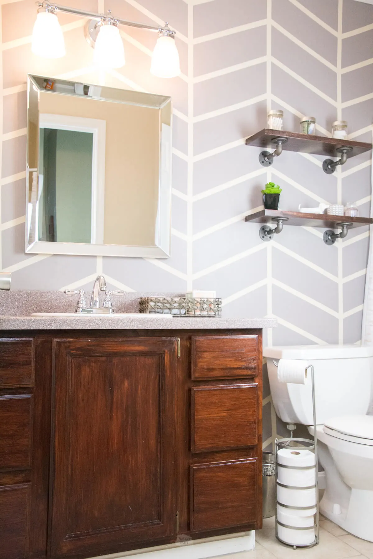 gray herringbone painted bathroom accent wall with gel stained cabinets and industrial bathroom shelves.