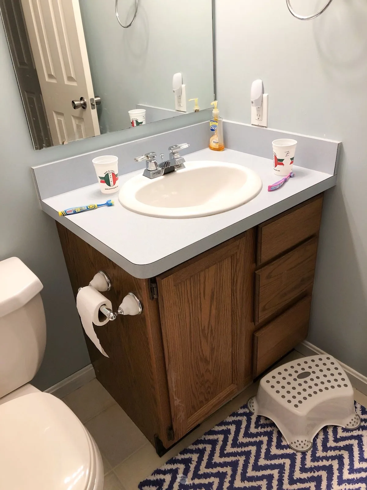 Oak bathroom vanity with blue laminate countertops, stool and carpet in small bathroom.