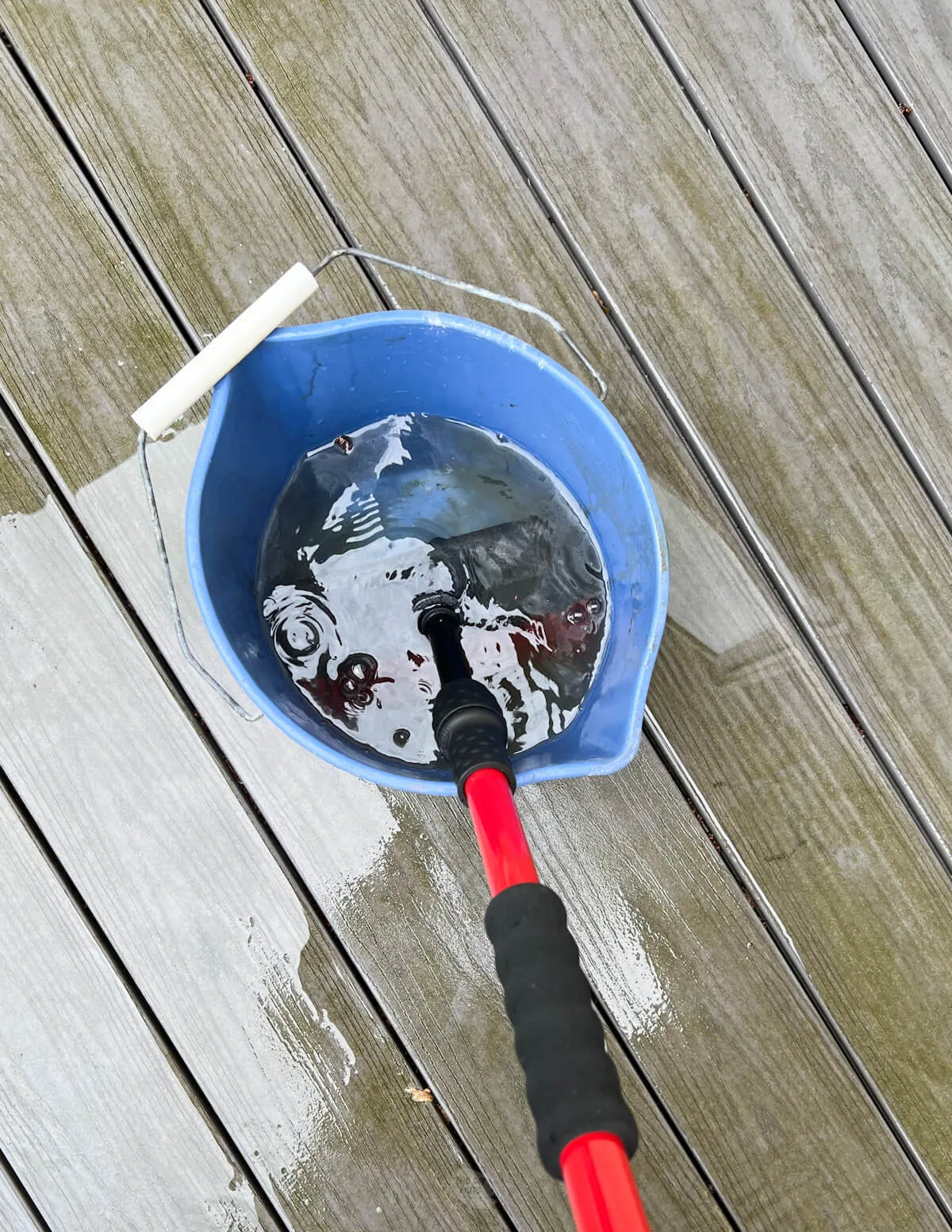 deck brush being put in DIY cleaning solution in blue bucket.