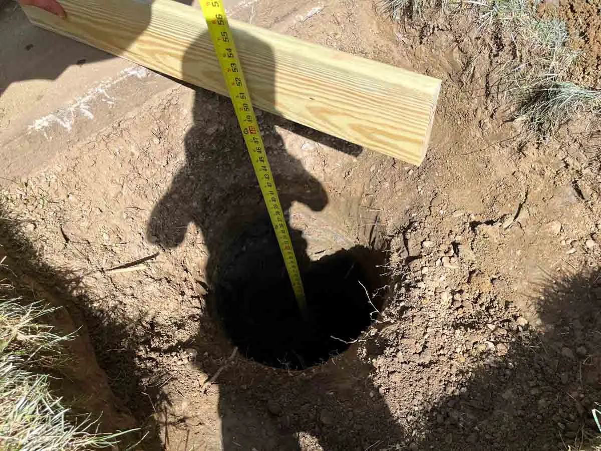 man holding 2 x 4 with tape measure in hole in the ground.
