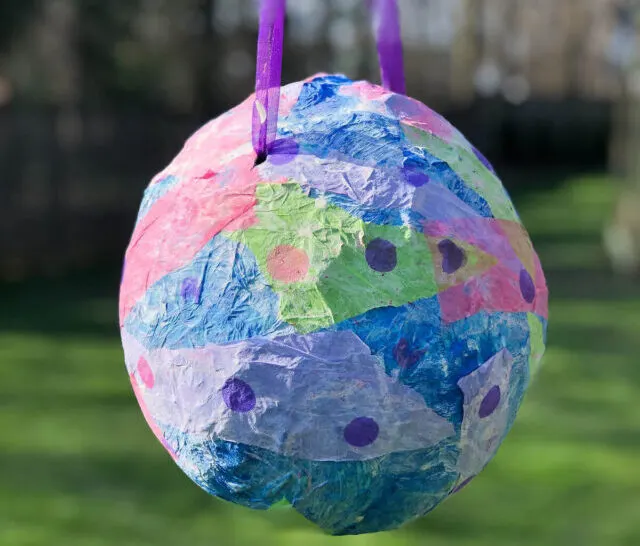 colorful homemade piñata made from a balloon hanging outside.