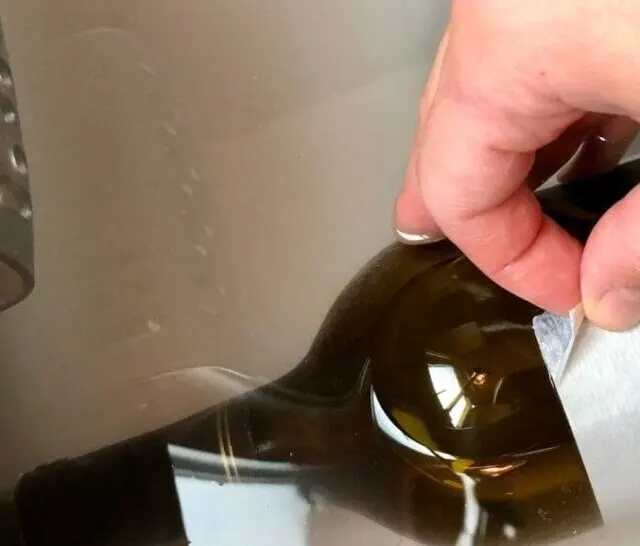 wine label being removed by hand and bottle soaking in baking soda