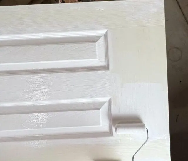 hand holding small roller painting across bottom of door.