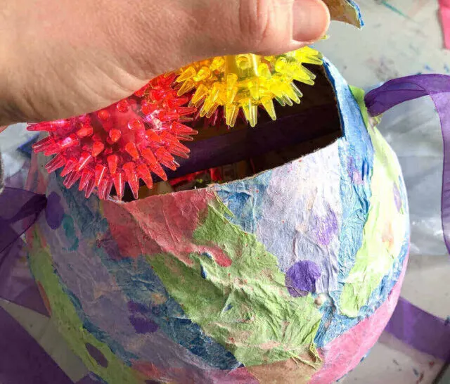 hand placing red and yellow spiky ball toy inside color piñata.