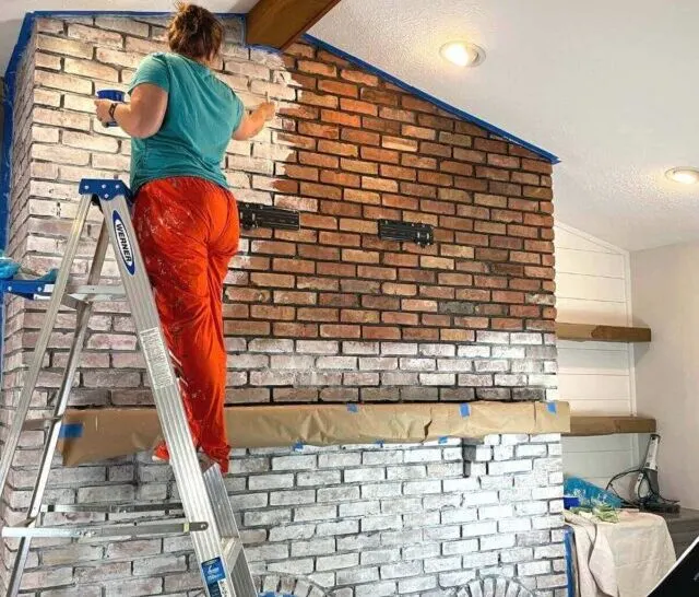 women standing on ladder whitewashing a brick fireplace.