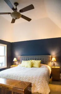 gray headboard on bed with navy blue walls and fan on the ceiling.