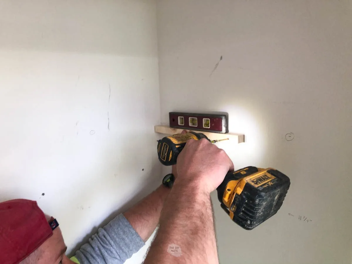 man attaching wooden closet bracket with drill, screw and torpedo on top.
