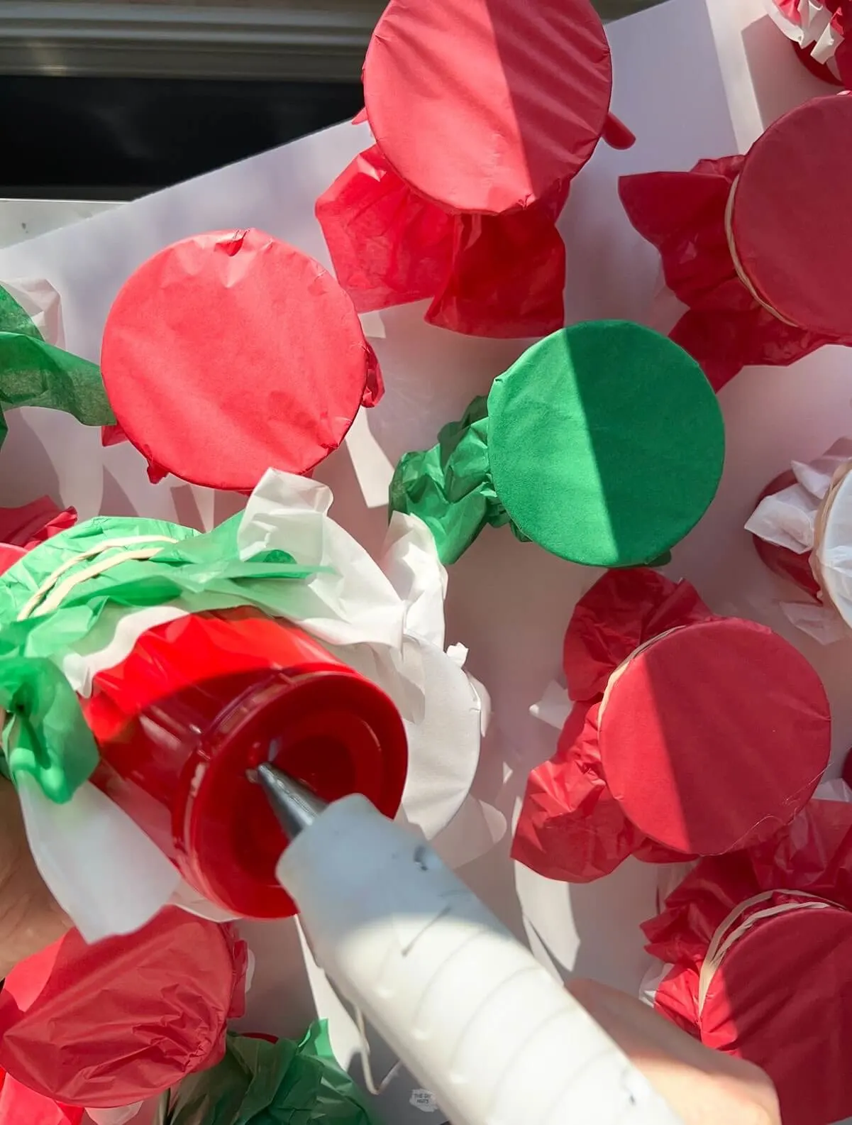 hot glue gun added hot glue to the bottom of a red cup with tissue paper cups in the background.