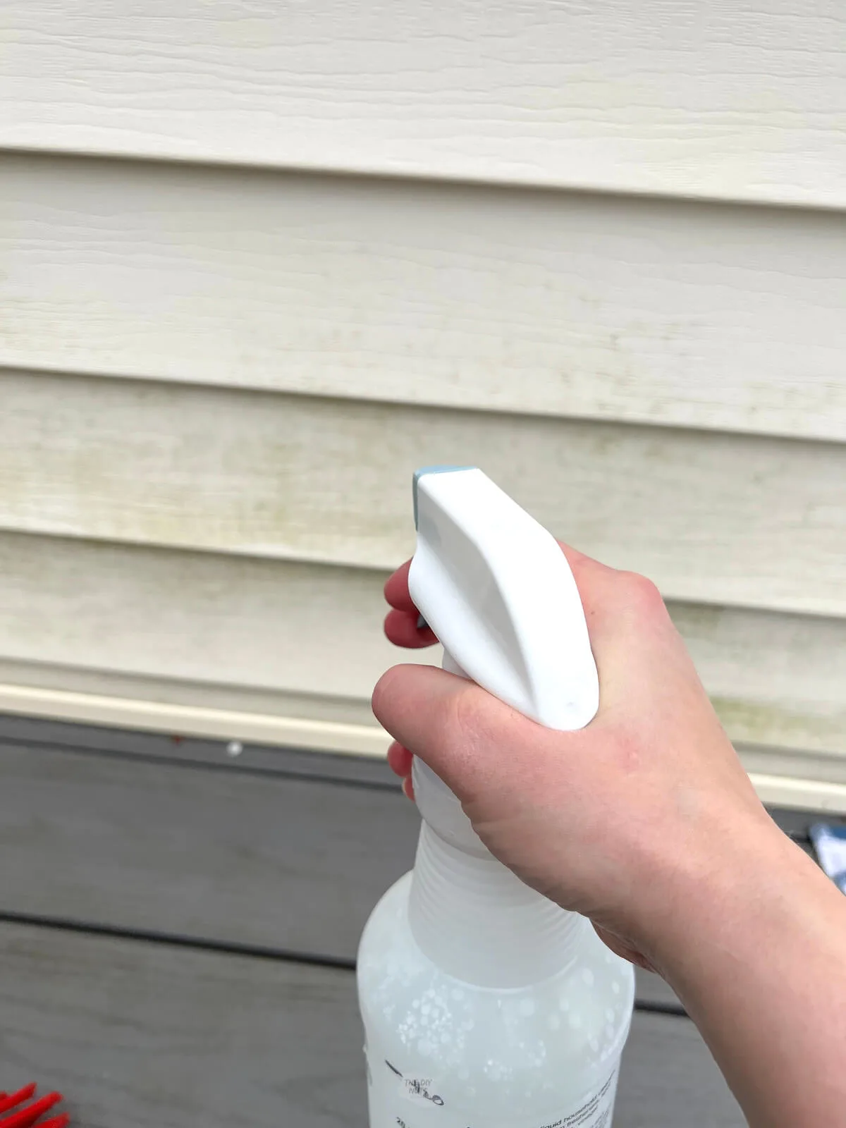 hand holdig spray bottle with white vinegar and water mixture to clean house siding.