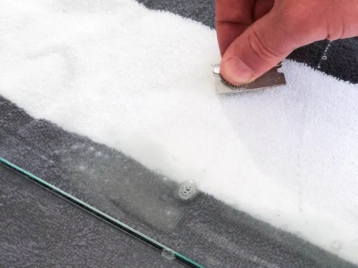 hand cleaning spray paint off glass with razor.