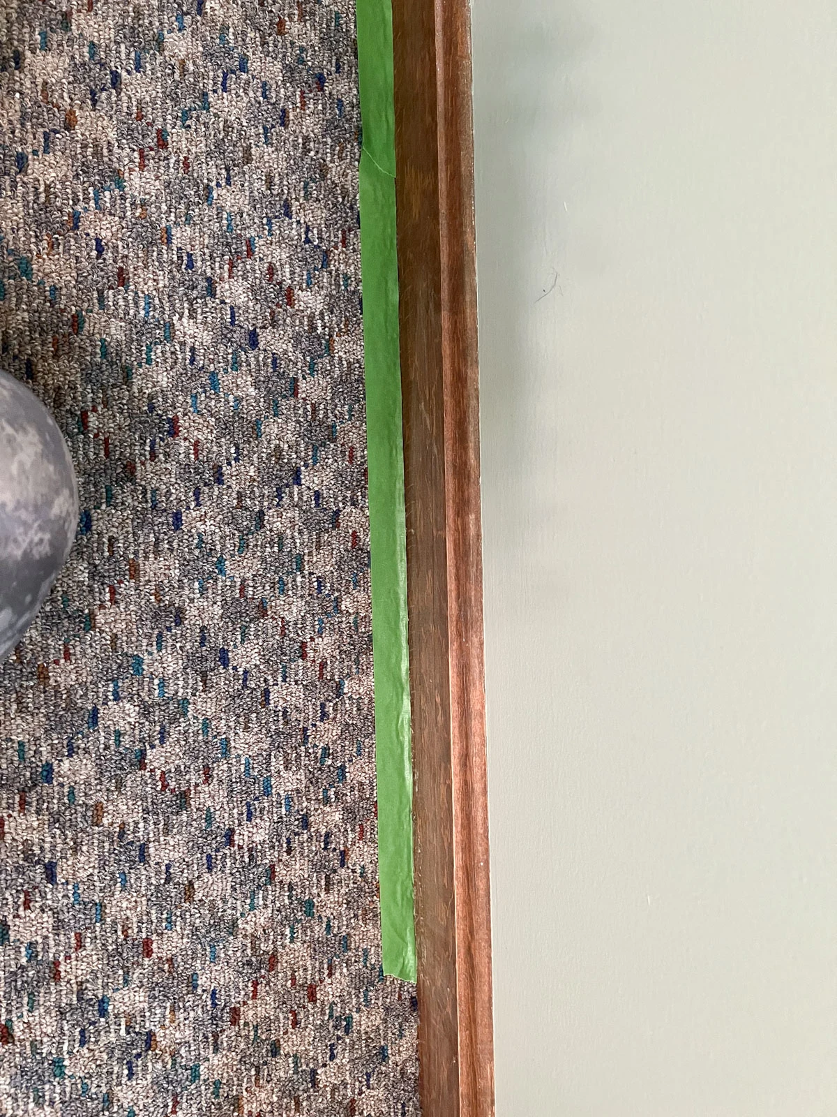 green painter's tape on carpet under wood baseboards.