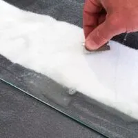 hand holding razor blade at 45 degree angle getting spray paint off glass.