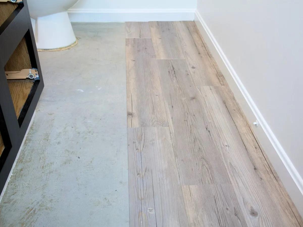 peel and stick vinyl planks on half of bathroom floor with toliet and vanity in the background.