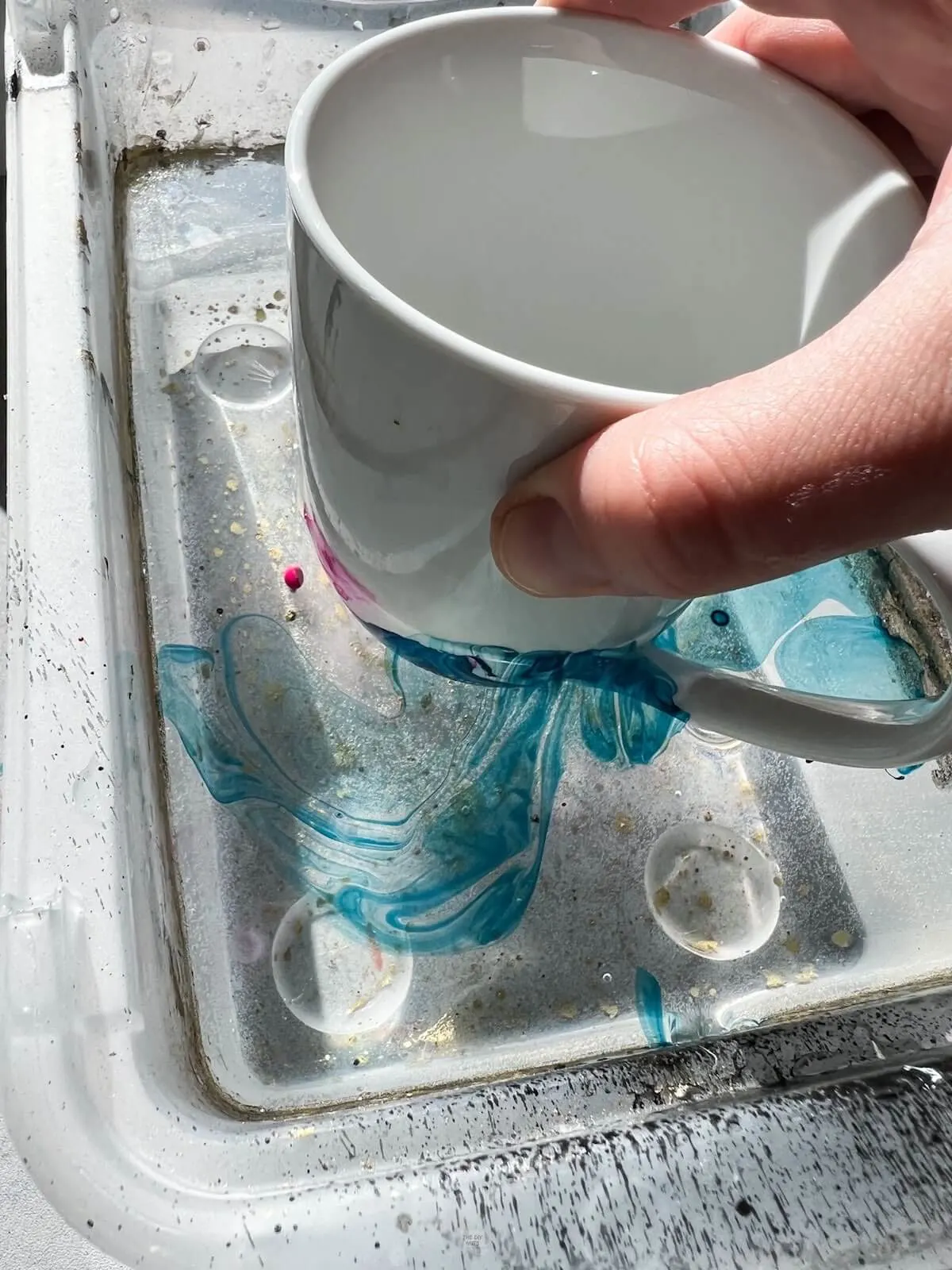 hand dipping mug in water with nail polish on top.