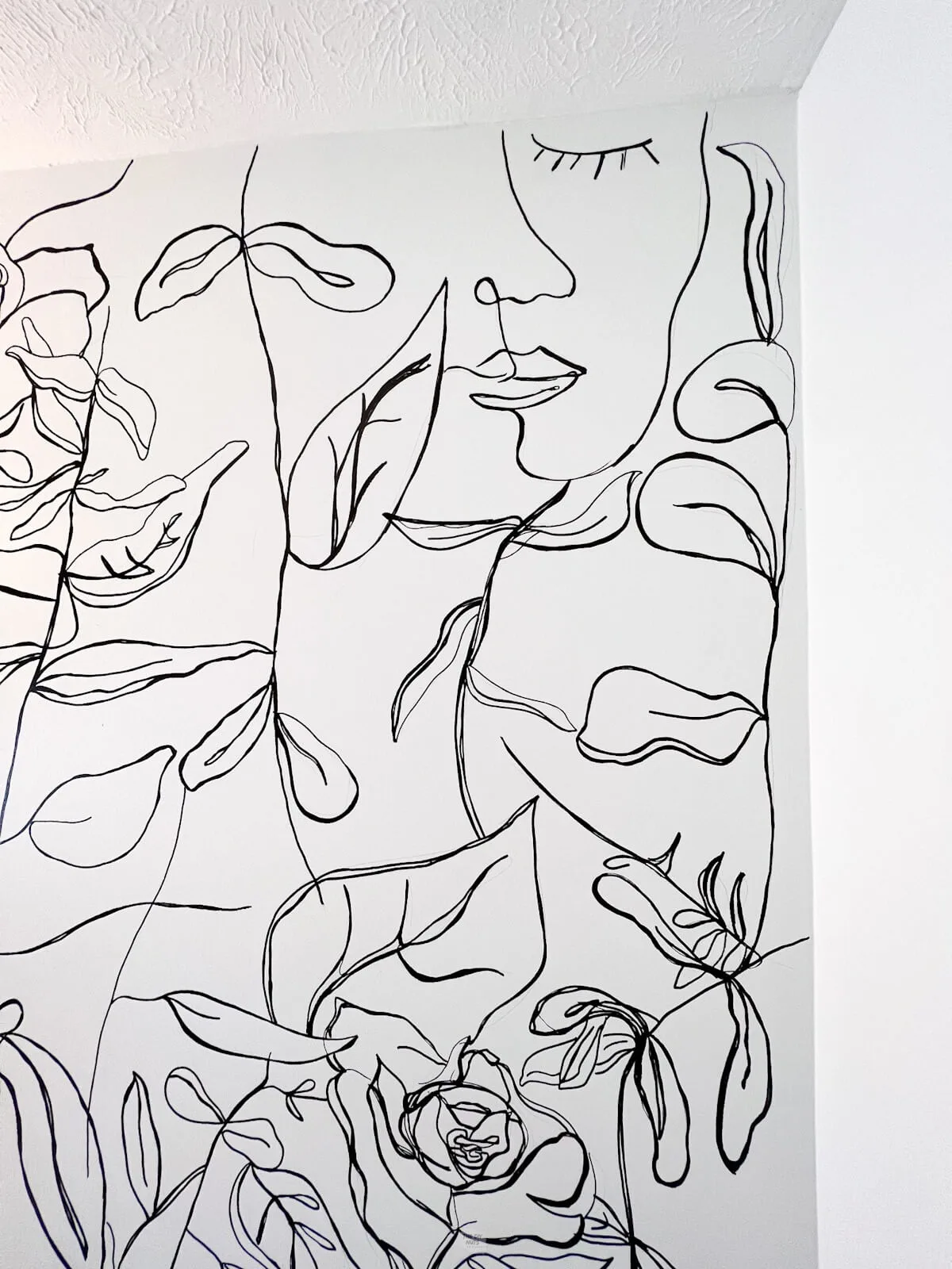 corner of a room with white walls and unique black line drawings of flowers, plants and a contour face.