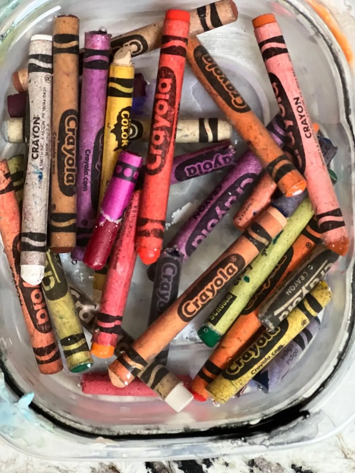 crayons soaking in water in small plastic container.