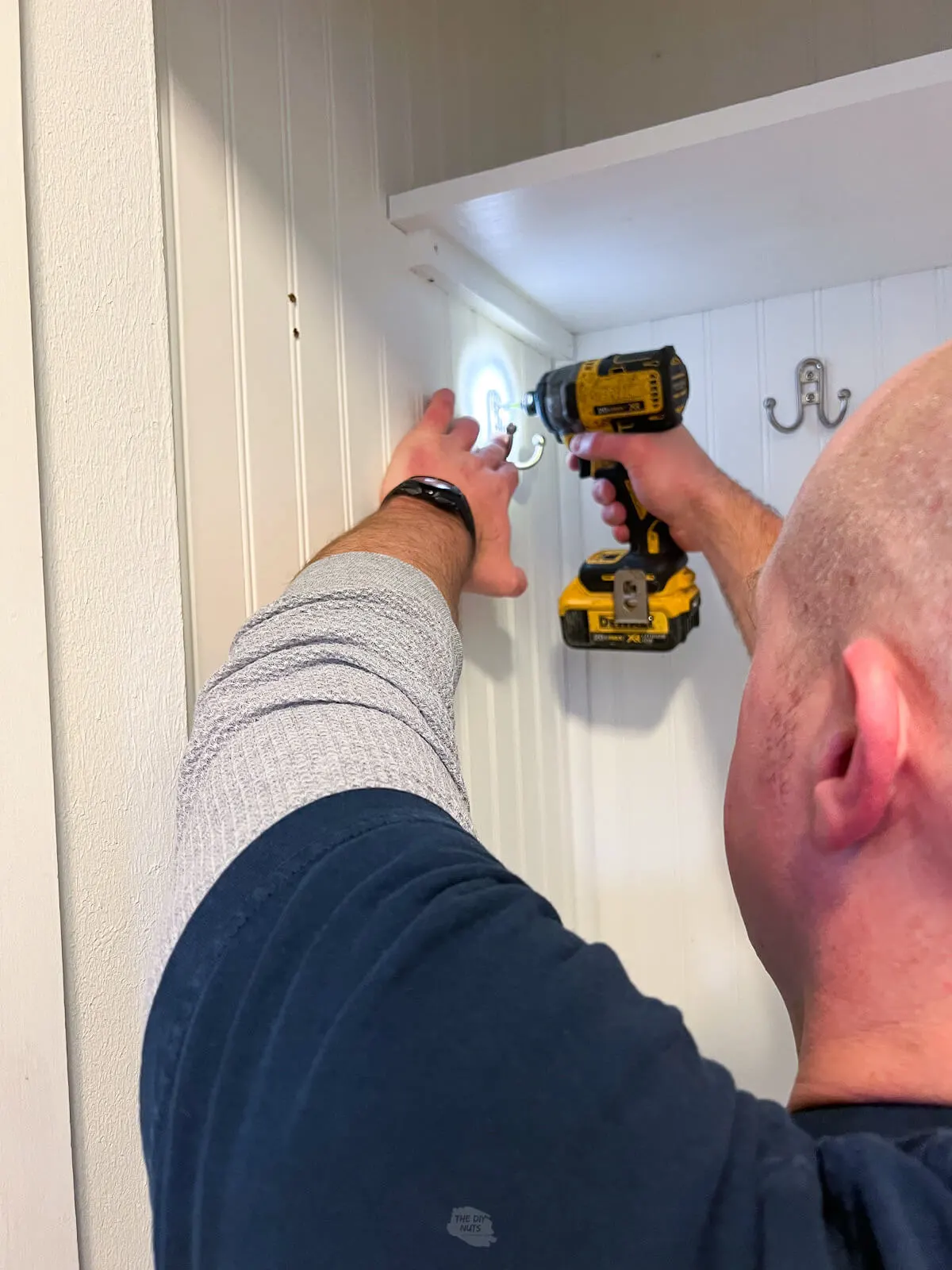 man removing hardware hooks with drill before painting begins of painted mudroom closet cubby.