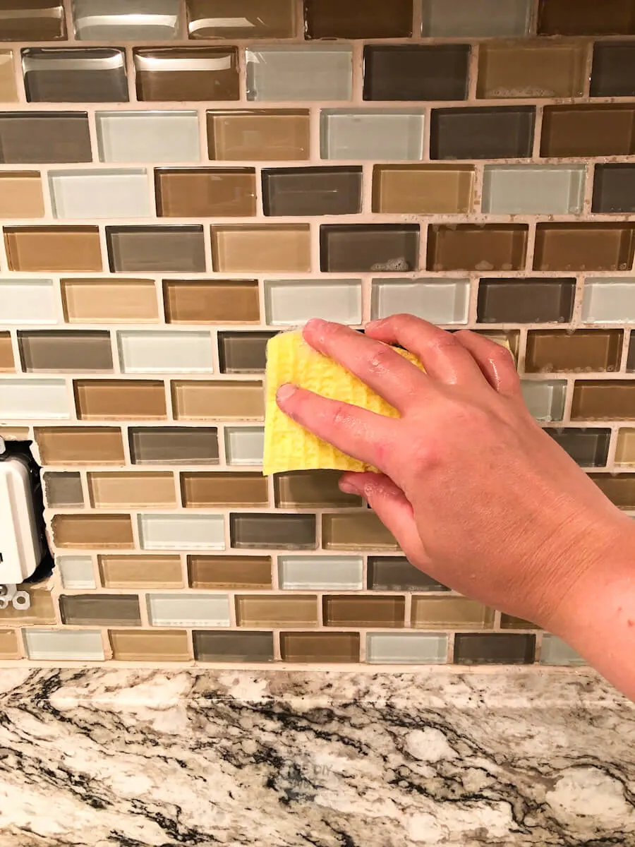 hand using sponge to clean and prep backsplash to be painted.