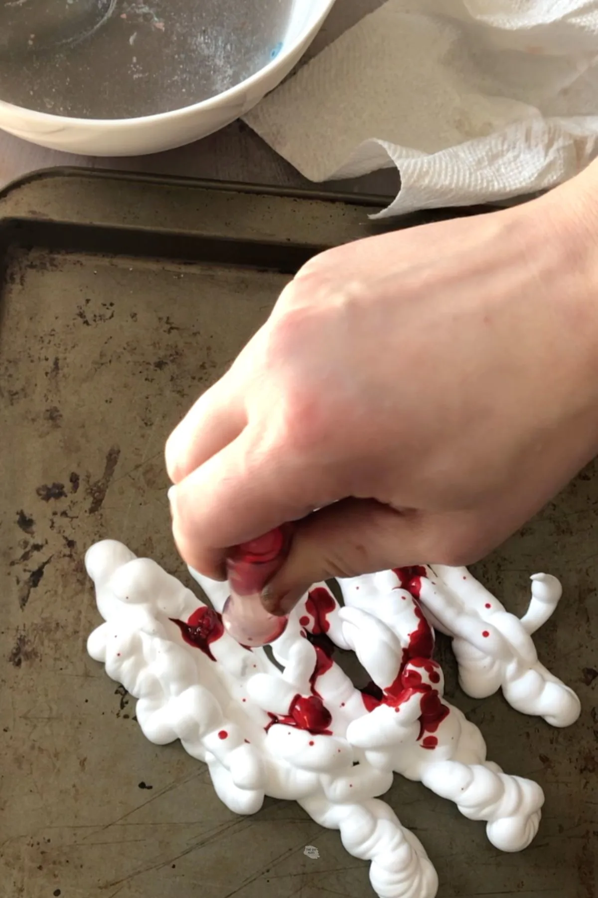 hand adding food coloring to shaving cream on cookie sheet.
